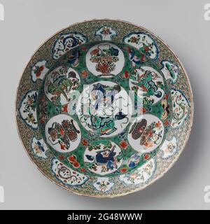 Plat avec animaux (mythologiques), paniers de fleurs et plantes à fleurs. Plat de porcelaine, peint sur le glaçage en bleu, rouge, vert, jaune, aubergine, noir et or. L'appartement est recouvert de branches de fleurs et de papillons sur un fond vert drainé noir. Voici un médaillon avec deux shishi (chien de lion) et un des objets de valeur (pièce). Ce médaillon est entouré de six médaillons avec alternance d'un panier de fleurs ou d'un shishi dans un paysage. Sur le bord de la serviette de travail avec différentes cartouilles en forme avec alternant un papillon, une plante à fleurs ou un chilong (dragon sans maïs). L'arrière Banque D'Images