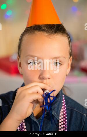 Jeune fille soufflant corne de fête pendant la fête d'anniversaire Banque D'Images