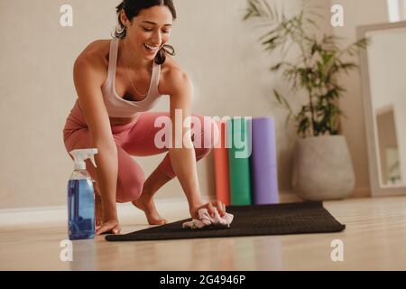 Femme utilisant un chiffon humide et un assainisseur de la bouteille pour nettoyer le tapis de yoga dans la salle de gym. Femme désinfectant tapis d'entraînement dans le studio de fitness. Banque D'Images