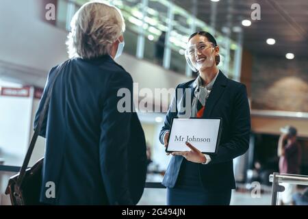 Chauffeur privé portant un masque de protection debout à l'aérogare, tenant une pancarte et recevant un voyageur. Femme chauffeur avec une pancarte à l'aéroport Banque D'Images