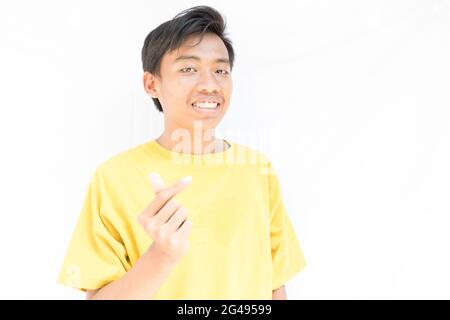 Un homme indonésien avec un t-shirt jaune montrant avec joie le geste d'amour coréen sur un fond blanc Banque D'Images