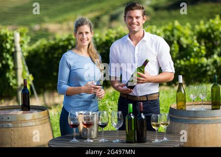 Portrait d'amis tenant des verres de vin et une bouteille à table contre le vignoble Banque D'Images