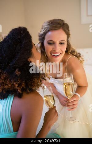 Chuchotant à l'oreille mariée de demoiselle tout en ayant une chambre en champagne Banque D'Images