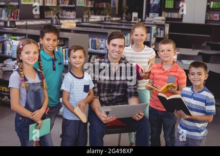 Portrait d'enseignant et d'écoliers à l'aide d'un ordinateur portable dans la bibliothèque Banque D'Images