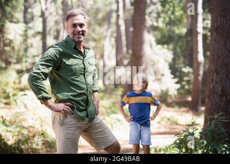 Père et fils avec les mains sur les hanches debout dans la forêt Banque D'Images