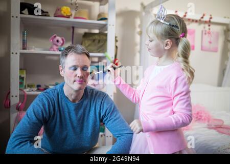 Jolie fille en costume de fée mettant le maquillage sur le visage de son père Banque D'Images