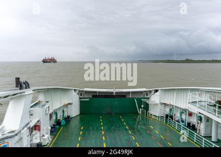 Vue de l'avant d'un ferry qui traverse la rivière Elbe avec un gros navire de fret à conteneurs Banque D'Images