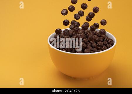 Chocolat balles de maïs tombant dans un bol sur fond jaune Banque D'Images