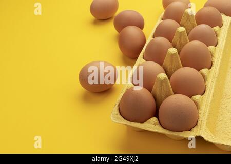 Oeufs de poulet brun dans une boîte en carton sur fond jaune, vue de dessus Banque D'Images