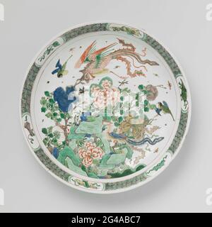 Soucoupe-plat avec rochers, fleurs et Feng Huangs. Plat avec paroi ronde et étalant de porcelaine, peint en bleu sous-glaçure et au-dessus du bleu, rouge, vert, jaune, aubergine et noir. Sur les rochers plats avec des branches fleuries et deux teintes feng, d'autres oiseaux et des insectes; le bord avec le modèle géométrique entrecoupé avec des symboles chanceux (castanets, scepter, rouleaux de livre, pierre de musique, feuille d'artemisia) dans les cartouris. Le fond avec trois branches de fleur. Marqué d'un repère de joint dans un double cercle. Quatre copeaux dans le bord. Famille verte. Banque D'Images