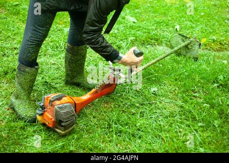 La tondeuse soulève la tondeuse. Jardinier équipé d'un outil pour couper l'herbe. Le travailleur prend une tondeuse à essence. Banque D'Images