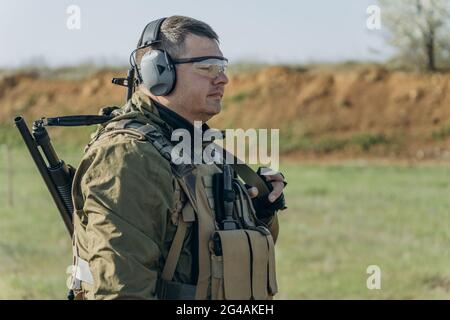 armé jeune homme blanc en uniforme militaire portant des écouteurs et des lunettes sur le terrain d'entraînement Banque D'Images