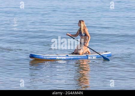 Une jeune femme s'agenouille sur son paddle-board sur une mer bleue calme. Banque D'Images
