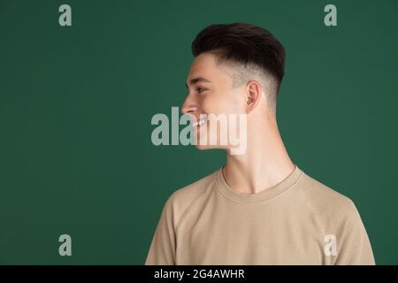 Portrait d'un jeune garçon caucasien isolé sur fond vert de studio. Concept des expressions faciales, des émotions humaines. Banque D'Images