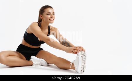 Sport et entraînement. Jogging souriant, athlète féminine faisant des exercices d'étirement à l'intérieur, arrière-plan blanc isolé. Sportswoman taille sa jambe, extensible pour Banque D'Images