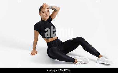 Sportswoman dans les vêtements de sport reposant sur le sol, après avoir fait une pause de jogging. Blonde sport fille prend la pause entre les exercices d'entraînement, session d'entraînement dans Banque D'Images