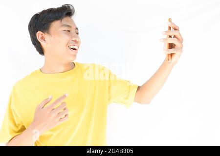 Un indonésien avec un t-shirt jaune se réjouit de passer un appel vidéo sur son téléphone sur fond blanc Banque D'Images