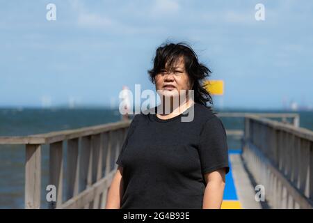 Une femme asiatique d'âge moyen sur une jetée avec un océan bleu et le ciel en arrière-plan. Photo du comté de Scania, Suède Banque D'Images