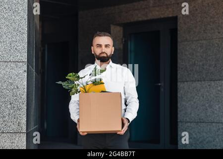 Contrarié homme d'affaires mature debout à l'extérieur avec une boîte de trucs. Le taux de chômage augmente et le concept de réduction du personnel Banque D'Images