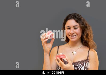 Portrait d'une fille souriante tenant une prothèse avec fond gris. Banque D'Images