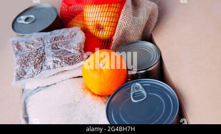 Boîtes de conserve, fruits frais aux pommes, sarrasin et riz dans une boîte en carton. Don d'aliments, thème de livraison. Banque D'Images