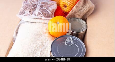 Boîtes de conserve, fruits frais aux pommes, sarrasin et riz dans une boîte en carton. Don d'aliments, thème de livraison. Banque D'Images