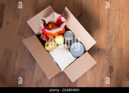 Boîtes de conserve, fruits frais aux pommes, sarrasin et riz dans une boîte en carton. Don d'aliments, thème de livraison. Banque D'Images