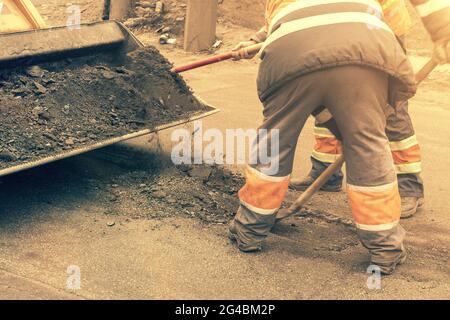 Les travailleurs de la route en uniforme réfléchissant orange vif utilisent des pelles pour gratter le sable accumulé. Entretien des chaussées et des chaussées. Réparation des nids de poule Banque D'Images