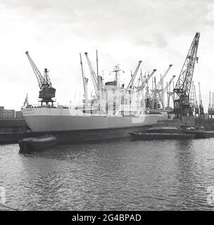 Années 1960, navire de fret grec historique, 'IKTINOS' amarré à Tilbury Docks sur la Tamise à Tilbury Essex, Angleterre, Royaume-Uni, une partie du port plus large de Londres. A côté de lui, la grue flottante de l'APL, London Léviathan, une barge de grue automotrice, construite à Amsterdam en 1965 pour l'Administration portuaire de Londres. Le cargo IKTINOS a été construit en juillet 1969 par Doxford & Sunderland Shipbuilding & Engineering Co., Ltd., Sunderland, Royaume-Uni, pour Linées Interoceanicas S.A. sous le drapeau grec. Banque D'Images