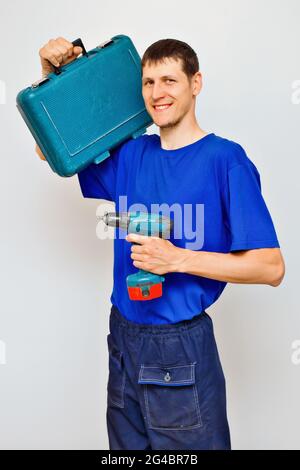Un jeune réparateur en combinaison tient un tournevis et une valise avec des outils et des sourires. C'est un bon travailleur. Service de réparation et d'entretien Banque D'Images