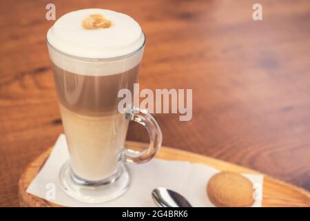 Café latte macchiato dans une tasse de café en verre transparent. La tasse est sur fond de bois avec un biscuit au café sur la table à côté du c Banque D'Images