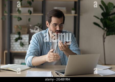 Jeune homme concentré enregistrant des messages audio sur un téléphone portable. Banque D'Images