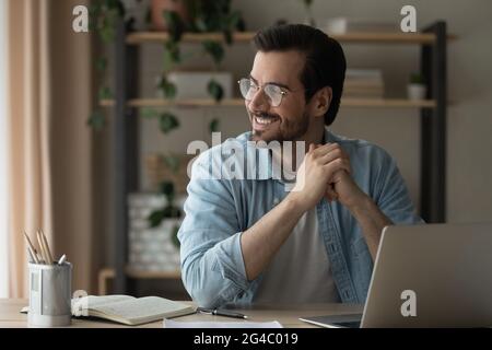 Jeune homme souriant dans des lunettes distrait du travail d'ordinateur. Banque D'Images