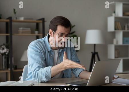 Un jeune homme en colère et confus regarde l'écran d'un ordinateur portable. Banque D'Images