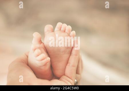 Mère tenant les pieds du nouveau-né dans sa main. Réglage en velours crémeux. Gros plan. Banque D'Images