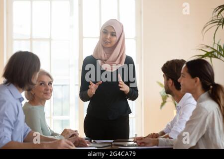 Femme d'affaires asiatique musulmane souriante, chef d'équipe, qui parle aux employés Banque D'Images