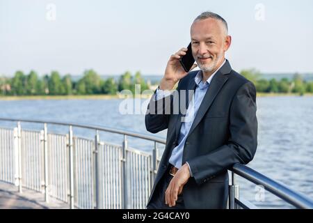 Homme d'affaires souriant dans un costume gris avec un smartphone. Banque D'Images