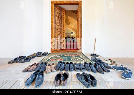 Chaussures déportées pour entrer dans la mosquée avec des gens qui prient en arrière-plan, Samarkand, Ouzbékistan Banque D'Images