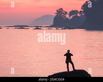 personne méconnaissable prenant des photos avec mobile au coucher du soleil sur un rocher aux îles de la grâce en espagne Banque D'Images