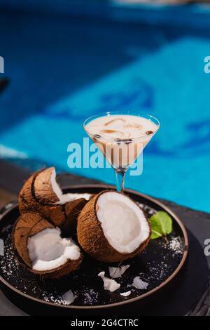 Café dans une tasse à côté de tranches de noix de coco servi sur le côté de la piscine. Boisson rafraîchissante d'été au bord de la piscine Banque D'Images