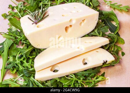 Tranches de fromage Maasdam avec feuilles d'arugula vertes sur fond de bois clair. Banque D'Images