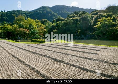 Kyoto, Japon - 18 septembre 2017 : jardin zen en pierre avec gravier ragé le long de l'étang au jardin Sogenchi au temple Tenryu-ji avec montagnes à backgrou Banque D'Images