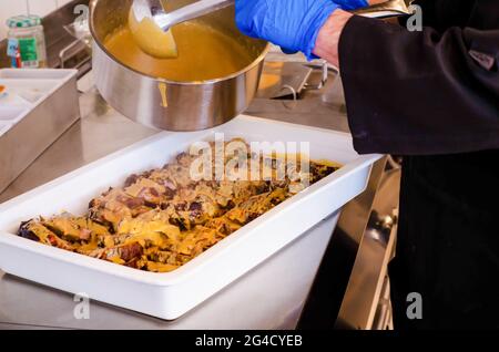 Un gros plan du chef qui verse de la sauce salée sur le filet de porc dans une casserole blanche Banque D'Images