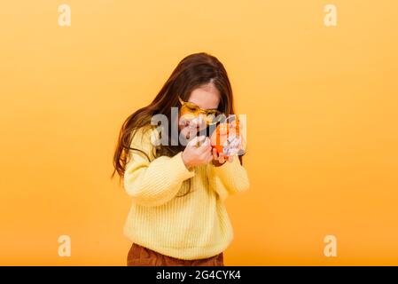 Il est temps de faire la fête. Un enfant mignon pensif tient un petit réveil dans ses mains. Studio jaune. Banque D'Images