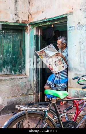 Un gentleman indien aux cheveux gris, lunettes et lunghi se tient dans le journal de lecture de porte, Gokarna, Karnataka, Inde Banque D'Images