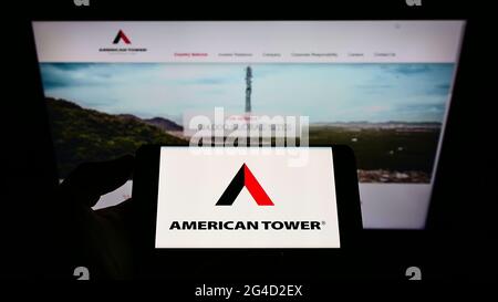 Personne tenant un téléphone portable avec le logo de la société d'infrastructure américaine American Tower Corp. À l'écran devant la page Web d'affaires. Mise au point sur l'affichage du téléphone. Banque D'Images