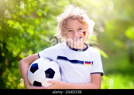 Les enfants jouent au football en plein air. Fans de l'équipe allemande avec drapeau national. Les enfants ont un but à un match de football. Enfant en jersey et crampons allemands Banque D'Images