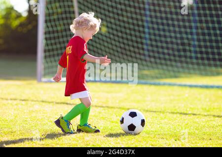 Les enfants jouent au football en plein air. Fans de l'équipe du Portugal. Les enfants ont un but à un match de football. Garçon en jersey portugais et crampons à frapper. Banque D'Images