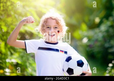 Les enfants jouent au football en plein air. Fans de l'équipe allemande avec drapeau national. Les enfants ont un but à un match de football. Enfant en jersey et crampons allemands Banque D'Images