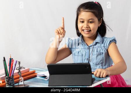 Une jolie petite fille indienne fréquentant un cours en ligne avec une tablette sur fond blanc Banque D'Images